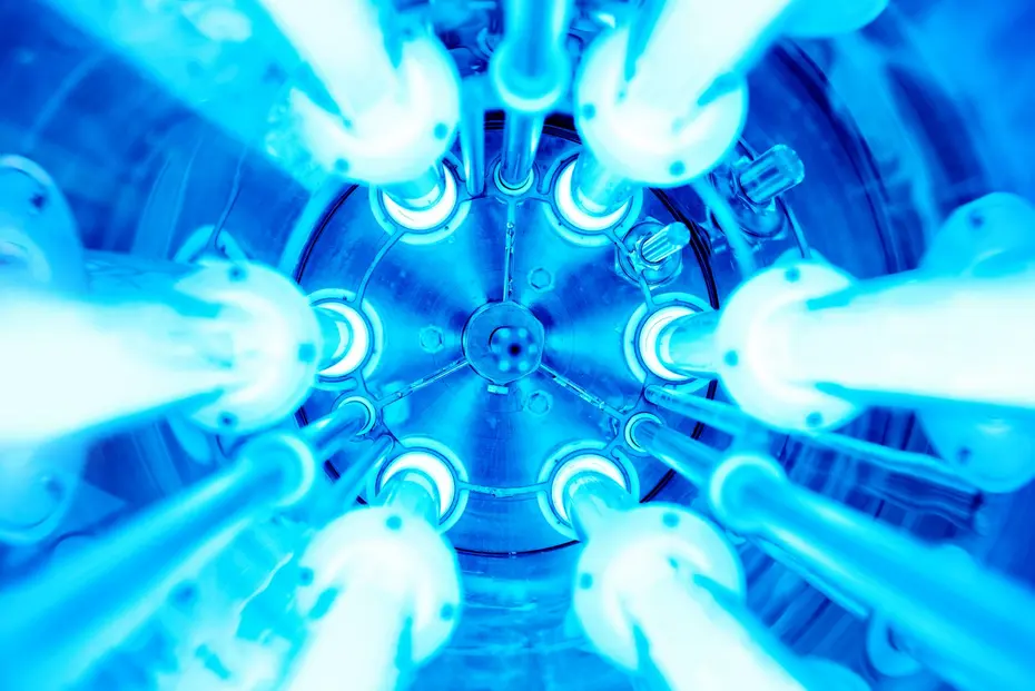 Eight circularly arranged, blue-glowing UV lamps inside a cylindrical reactor, viewed from below