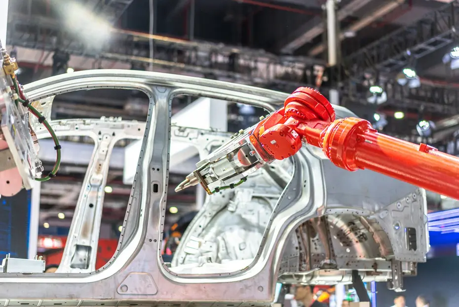Red industrial robot working on an unpainted vehicle body-in-white in automotive manufacturing