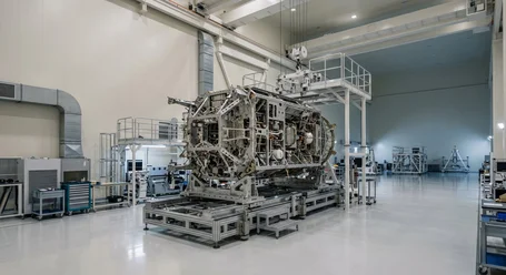 Aereo di linea e satellite sopra le nuvole, sotto di essi un emettitore LED UV su un componente in fibra di carbonio, accanto le icone qualità, affidabilità, processi certificati e innovazione – tecnologia UV per l'aerospaziale