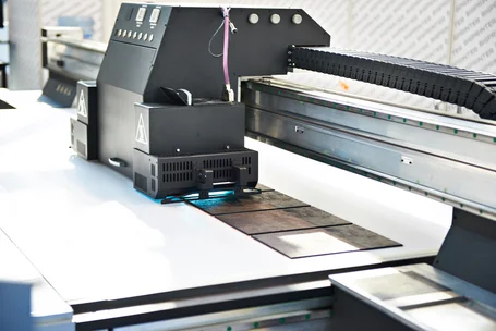 Dispositivo di misura UV sopra il nastro in movimento di una macchina da stampa con un'immagine stampata a quattro colori, accanto le letture di irradianza e dose – misurazione UV nella stampa offset, flessografica e serigrafica