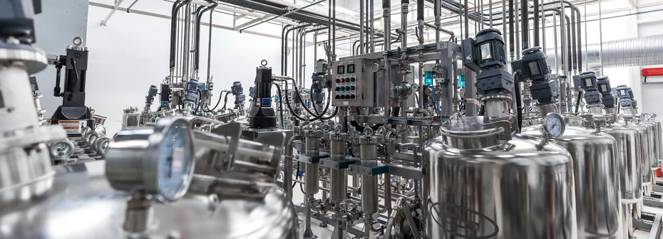 Chemical production plant with stainless steel reactors, agitator motors, piping, pressure gauges and a control cabinet in a bright pilot hall
